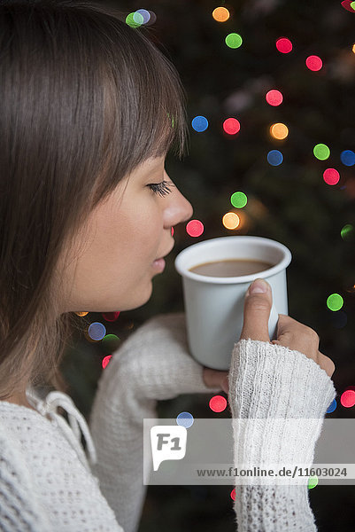 Gemischtrassige Frau trinkt Kaffee in der Nähe des Weihnachtsbaums