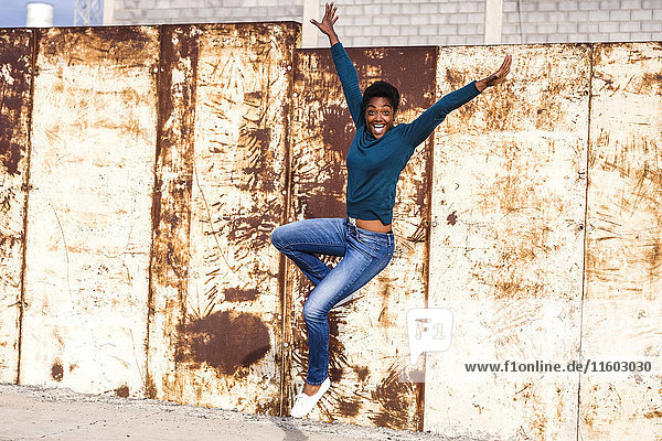 Vor Freude springende afroamerikanische Frau in der Nähe einer rostigen Metallwand