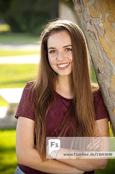 Portrait of smiling Caucasian teenage girl leaning on tree