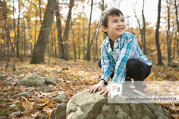 Lächelnder Mixed-Race-Junge  der im Herbst auf einem Felsen hockt