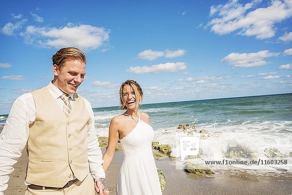 Caucasian bride and groom holding hands on beach
