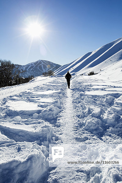 Kaukasischer Mann wandert auf einem Pfad im Schnee auf einem sonnigen Berg