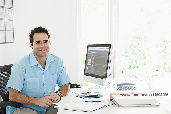 Porträt eines gemischtrassigen Mannes  der am Schreibtisch im Heimbüro sitzt