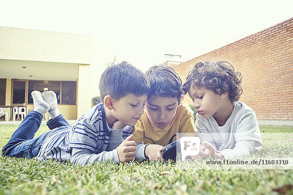 Hispanic boys laying in grass texting on cell phone