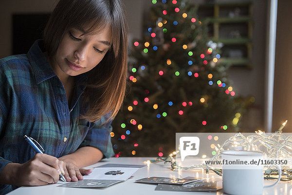 Gemischtrassige Frau schreibt auf Karte in der Nähe des Weihnachtsbaums