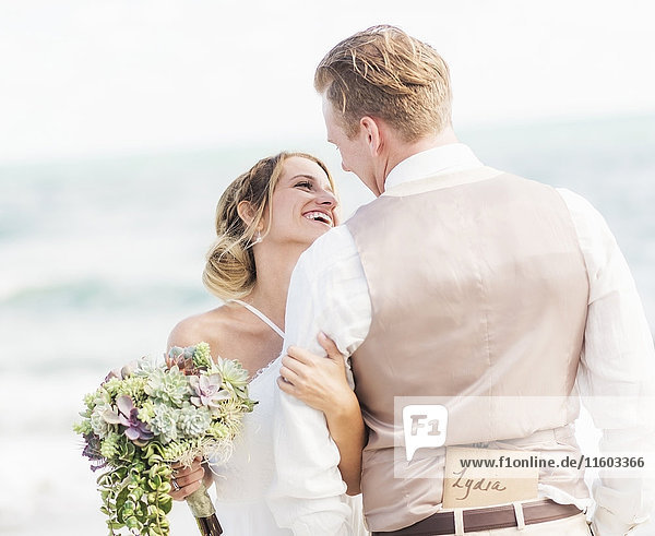 Caucasian bride and groom hugging on beach