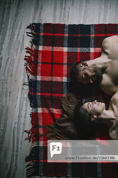 Caucasian couple laying face to face on plaid blanket