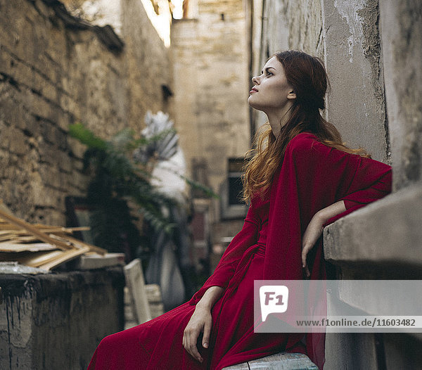 Kaukasische Frau in rotem Kleid sitzt auf einer Bank in einer Gasse
