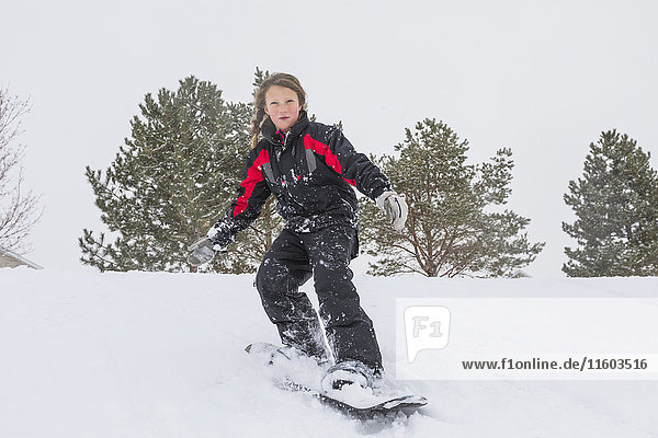 Serious girl riding snowboard on hill in winter