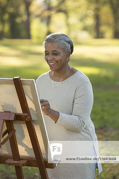 Schwarze Frau malt auf Leinwand im Park