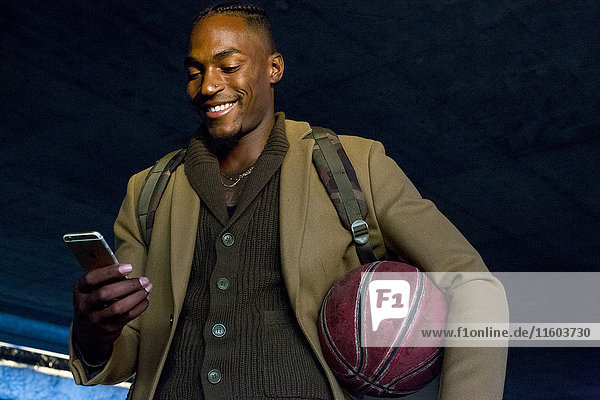 Schwarzer Mann hält Basketball und schreibt eine SMS auf seinem Handy