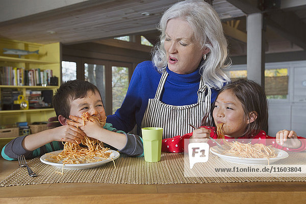 Großmutter beobachtet Enkel und Enkelin beim Spaghetti essen