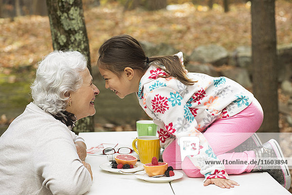 Großmutter und Enkelin spielen am Frühstückstisch im Freien