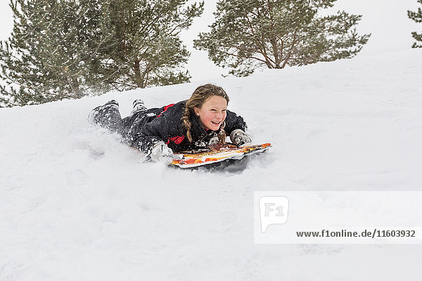 Lächelndes Mädchen gleitet auf dem Snowboard auf einem Hügel im Winter