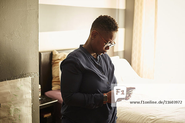 Schwarze Frau steht im Schlafzimmer und schreibt eine SMS mit ihrem Handy