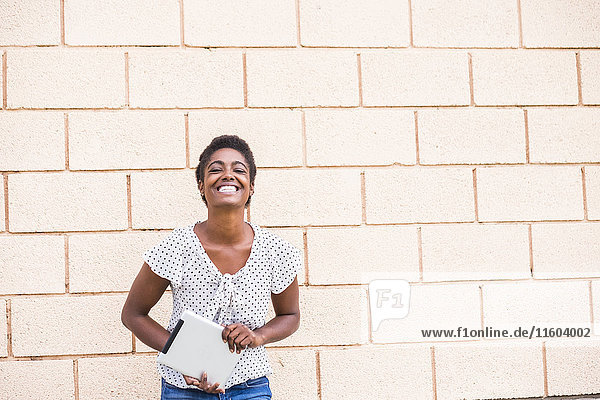 Lächelnde afroamerikanische Frau mit digitalem Tablet in der Nähe einer Betonwand