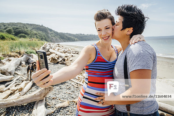 Schwangeres lesbisches Paar posiert für Handy-Selfie am Strand