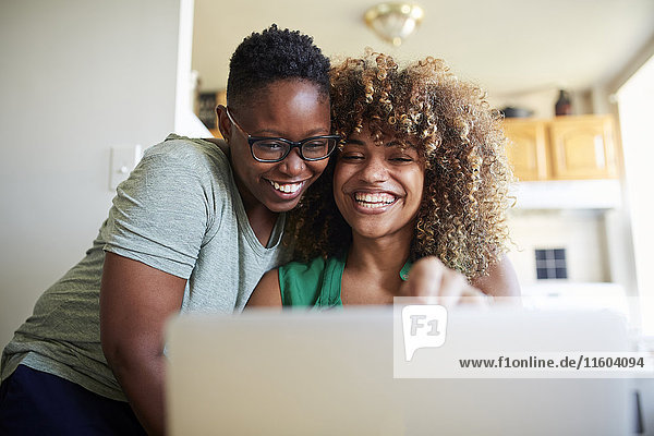 Lachende schwarze Frauen  die sich umarmen und einen Laptop benutzen