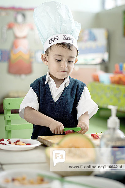 Hispanic boy cutting strawberry with plastic knife