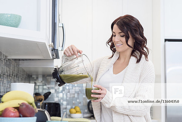 Kaukasische Frau gießt grünen Saft Smoothie in häuslicher Küche