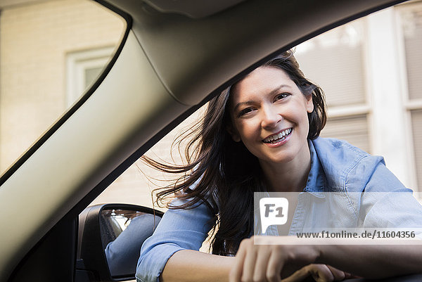 Lächelnde kaukasische Frau  die sich in ein Autofenster lehnt