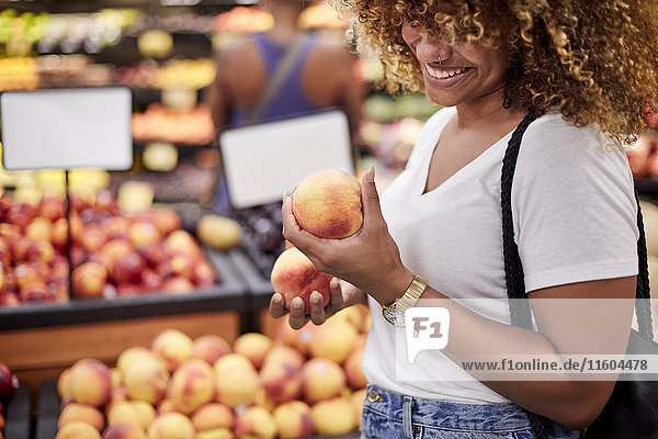Schwarze Frau begutachtet Pfirsiche im Lebensmittelgeschäft