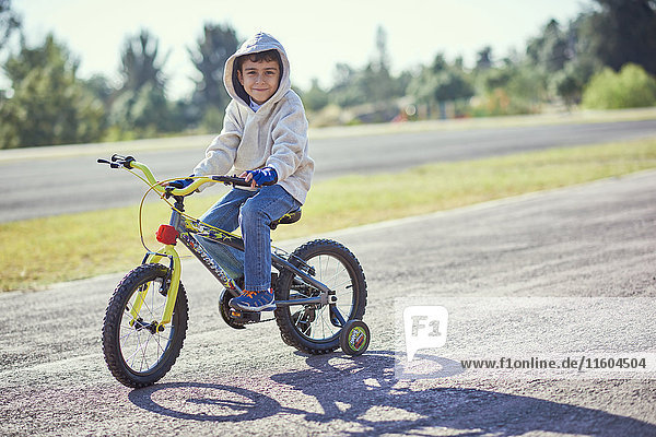 Hispanischer Junge posiert auf einem Fahrrad mit Stützrädern