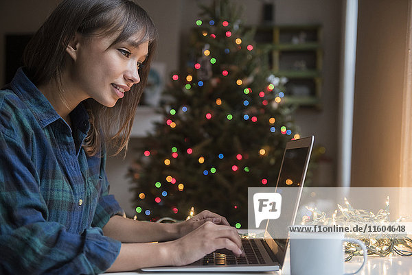 Gemischtrassige Frau benutzt Laptop in der Nähe des Weihnachtsbaums