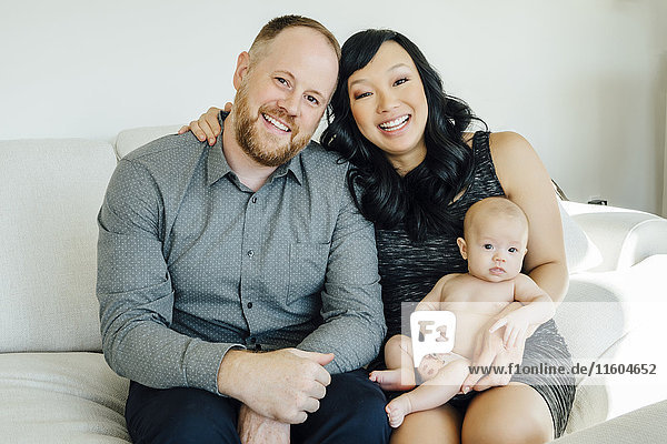 Portrait of smiling parents posing with baby daughter on sofa