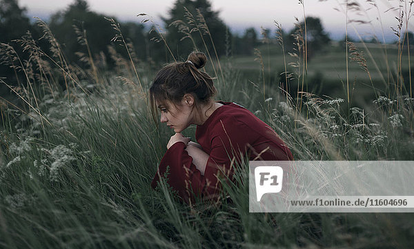 Nachdenkliche kaukasische Frau sitzt im hohen Gras