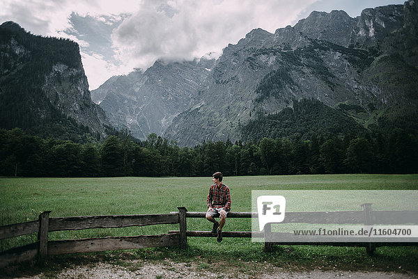 Caucasian man sitting on wooden fence near mountains