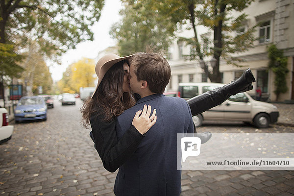 Kaukasischer Mann trägt und küsst Frau auf Kopfsteinpflasterstraße