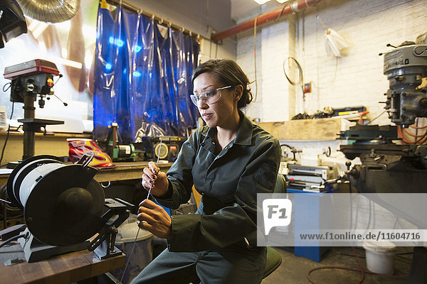 Gemischtrassige Frau hält Metallstange in Werkstatt