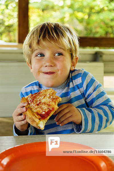 Playful Caucasian boy eating slice of pizza