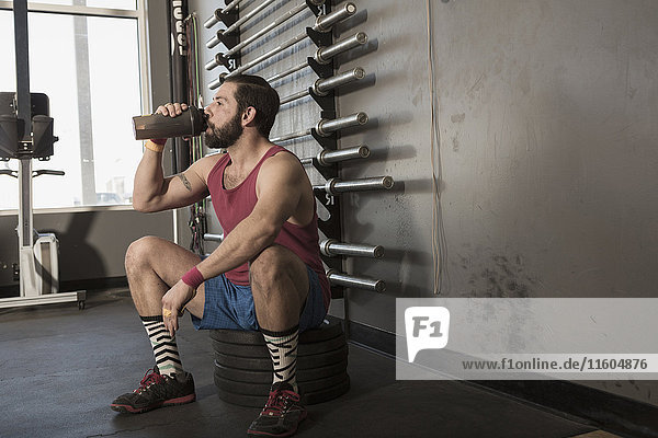 Mixed Race man drinking from bottle in gymnasium