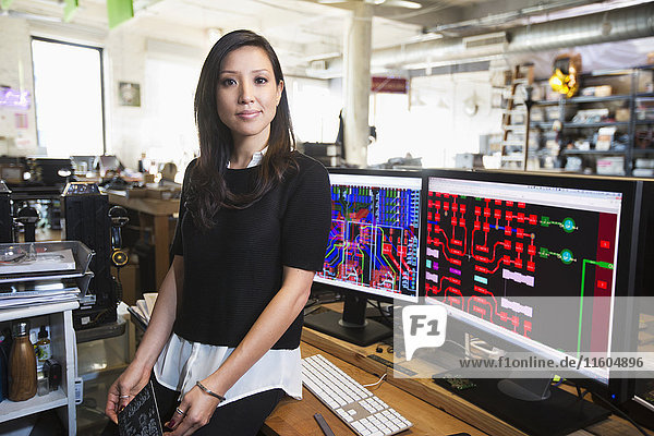 Gemischtrassige Frau posiert in der Nähe von Schaltkreisen auf Computermonitoren