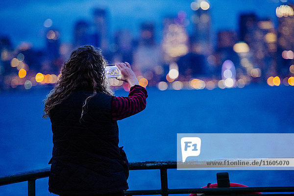Kaukasische Frau auf einem Boot  die mit ihrem Mobiltelefon das städtische Hafenviertel fotografiert