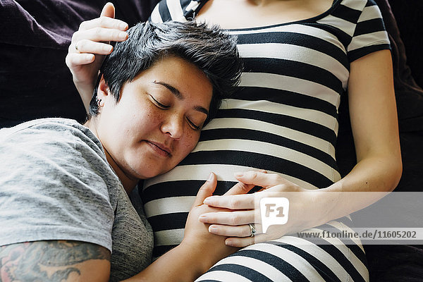 Pregnant lesbian couple cuddling on sofa