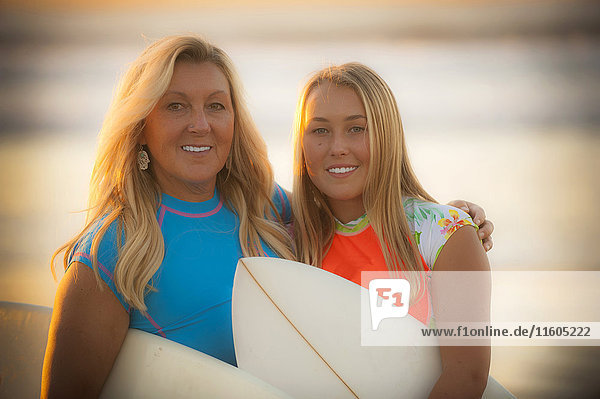 Porträt einer lächelnden kaukasischen Mutter und ihrer Tochter  die ein Surfbrett halten