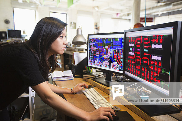 Mixed Race woman examining circuits on computer monitors