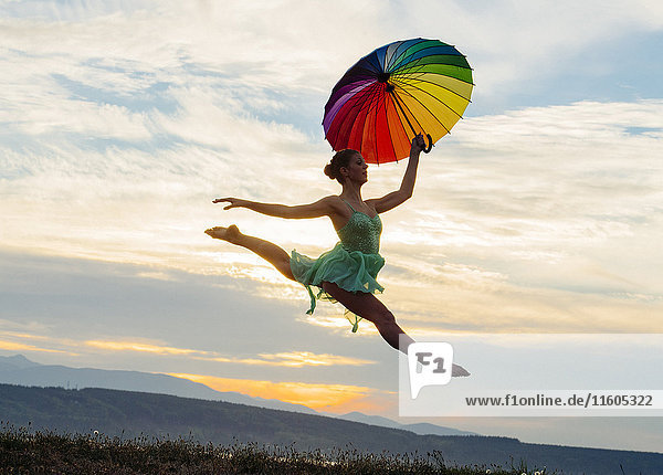 Caucasian ballerina jumping with multicolor umbrella