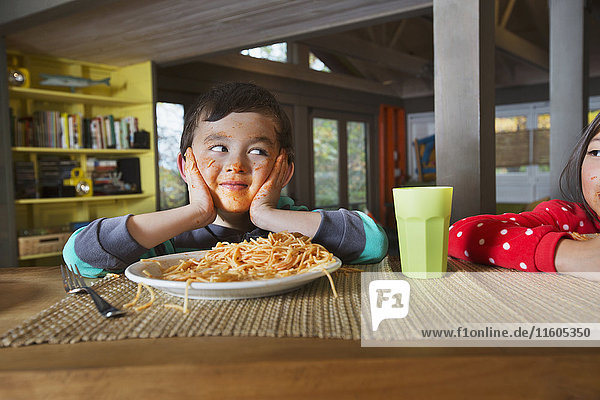 Schwester beobachtet Mixed Race Bruder mit unordentlichem Gesicht essen Spaghetti