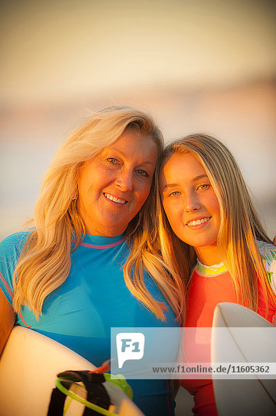 Porträt einer lächelnden kaukasischen Mutter und ihrer Tochter  die ein Surfbrett halten