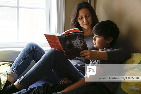 Mother and son reading book near window