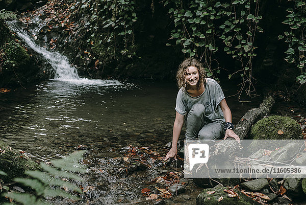 Caucasian woman crouching on rock in forest stream