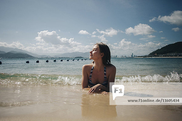 Kaukasische Frau im Bikini liegt in den Wellen am Strand