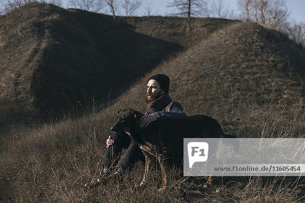 Kaukasischer Mann sitzt auf einem Hügel und streichelt einen Hund
