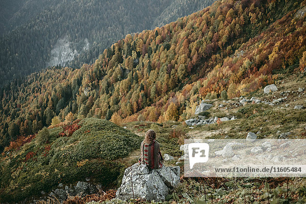 Kaukasische Frau sitzt auf einem Bergfelsen mit Blick auf ein Tal