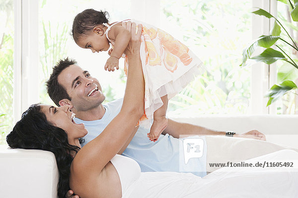 Mixed Race mother and father playing on sofa with baby daughter