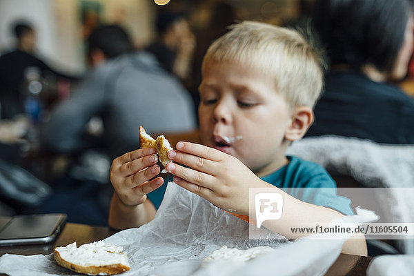 Gemischtrassiger Junge isst unordentlichen Bagel im Restaurant